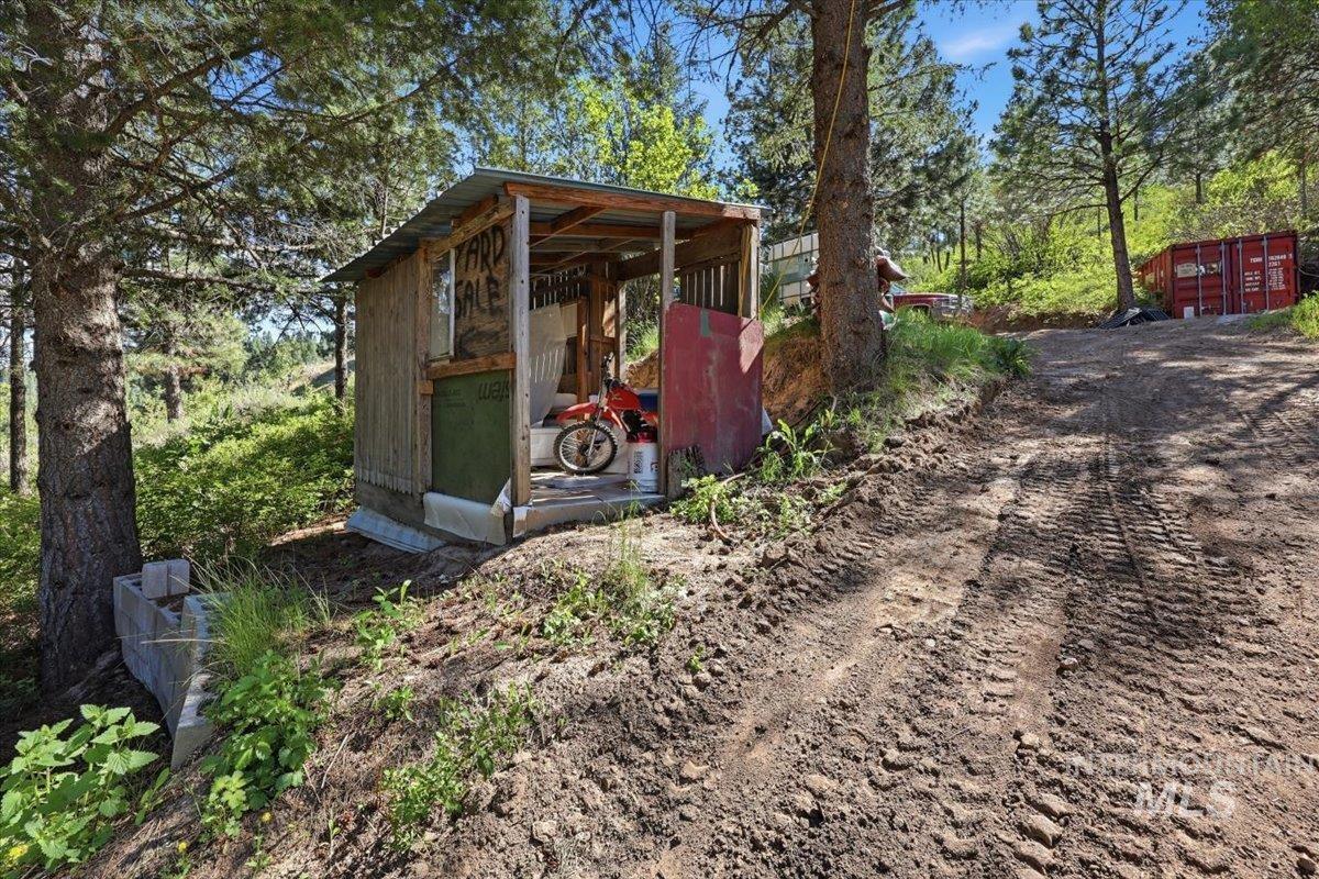 Rustic detached shed with open-front design and metal roof, positioned on a sloped, unpaved terrain