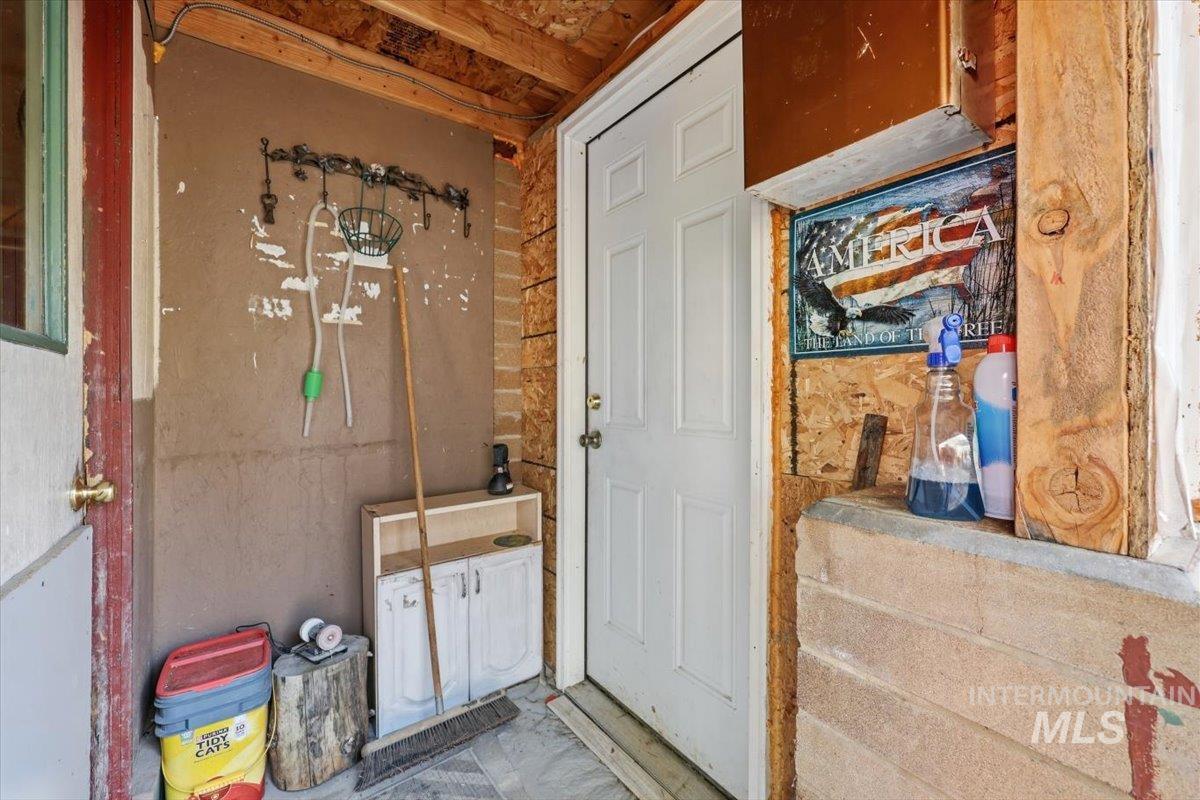 Covered porch area featuring a white paneled door, exposed wood ceiling beams, and concrete flooring