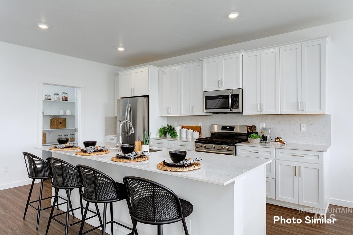 Kitchen with dark wood-type flooring, white cabinets, appliances with stainless steel finishes, a breakfast bar, and recessed lighting