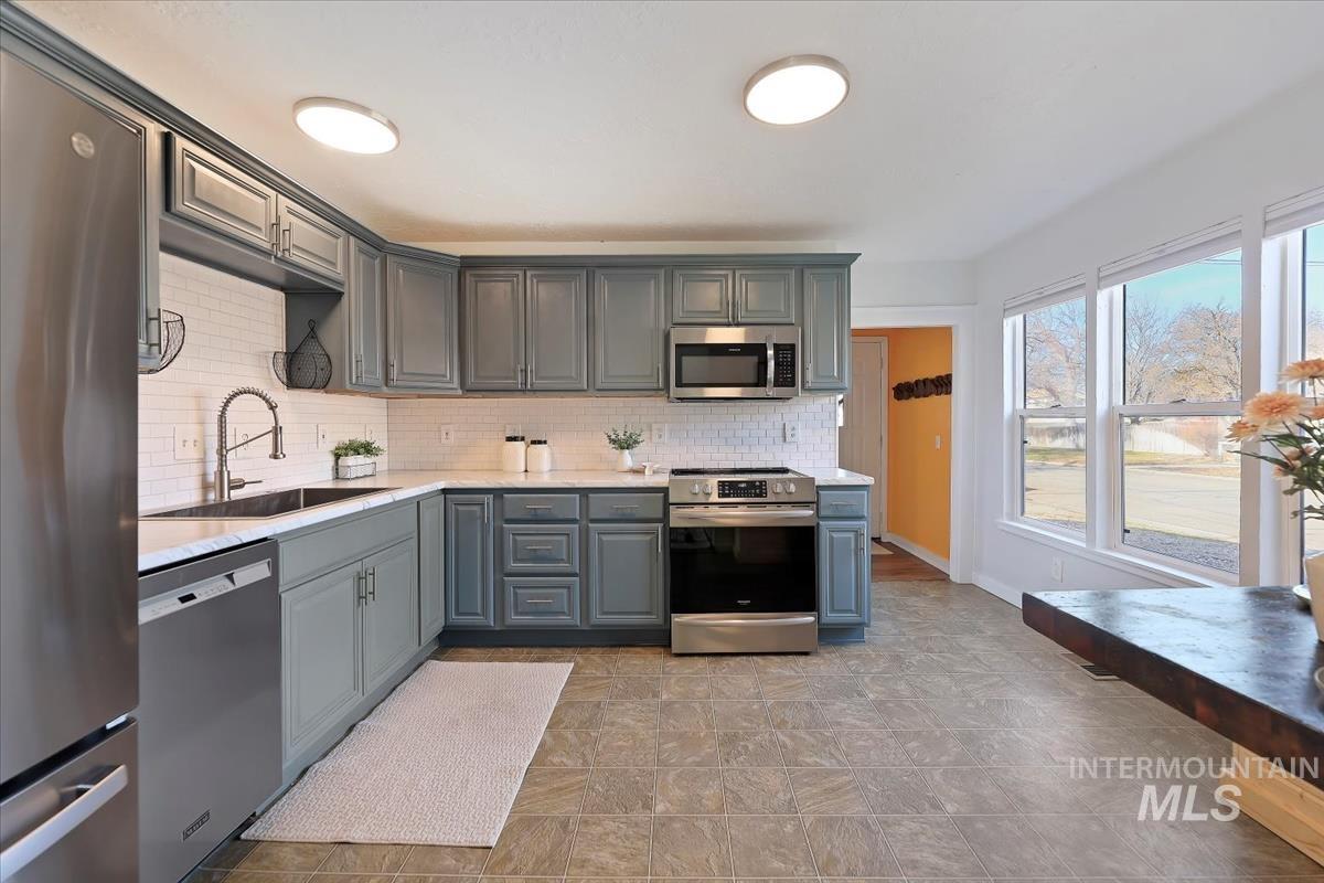 Kitchen featuring stainless steel appliances, gray cabinetry, backsplash, and light stone countertops
