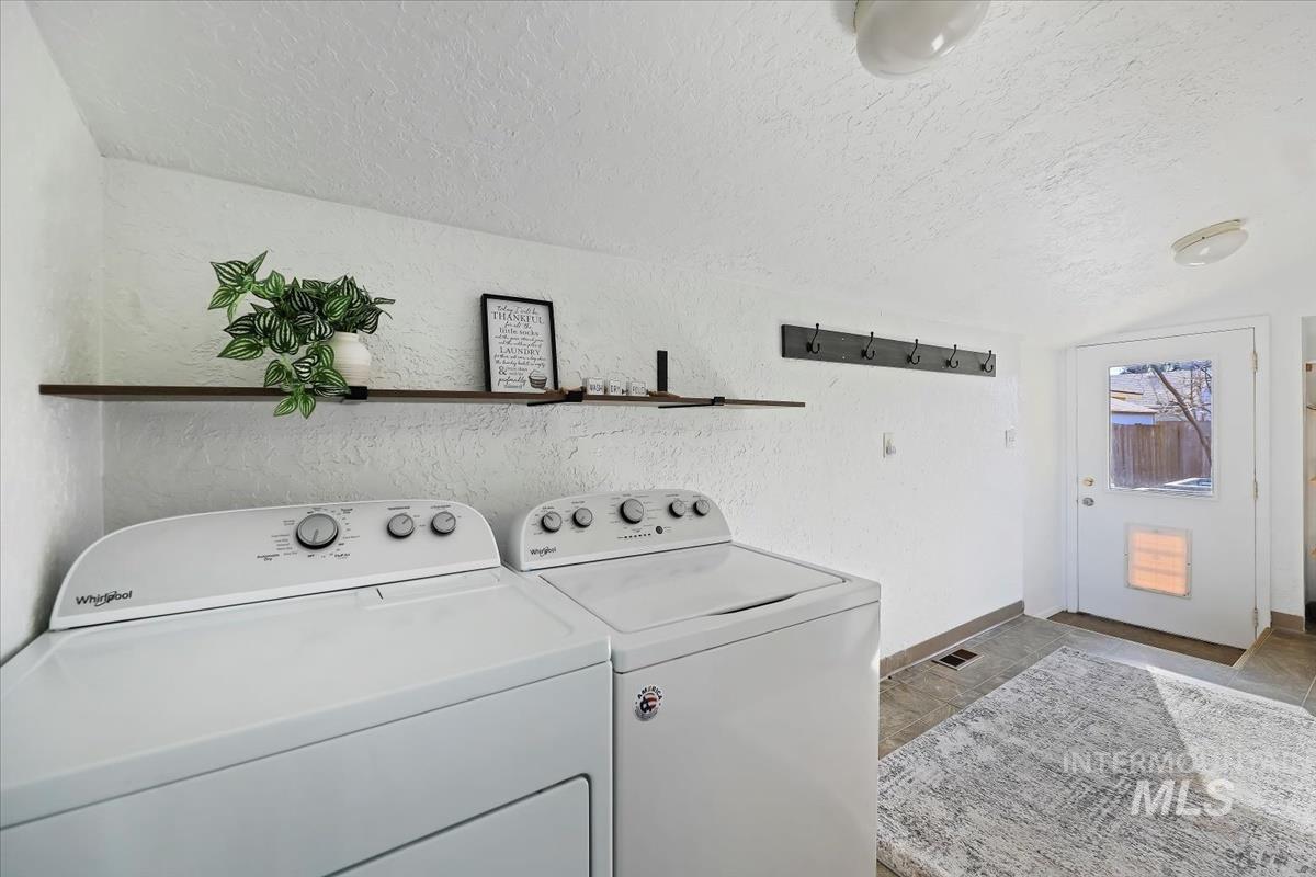 Laundry area with a textured wall, independent washer and dryer, and light stone finish flooring