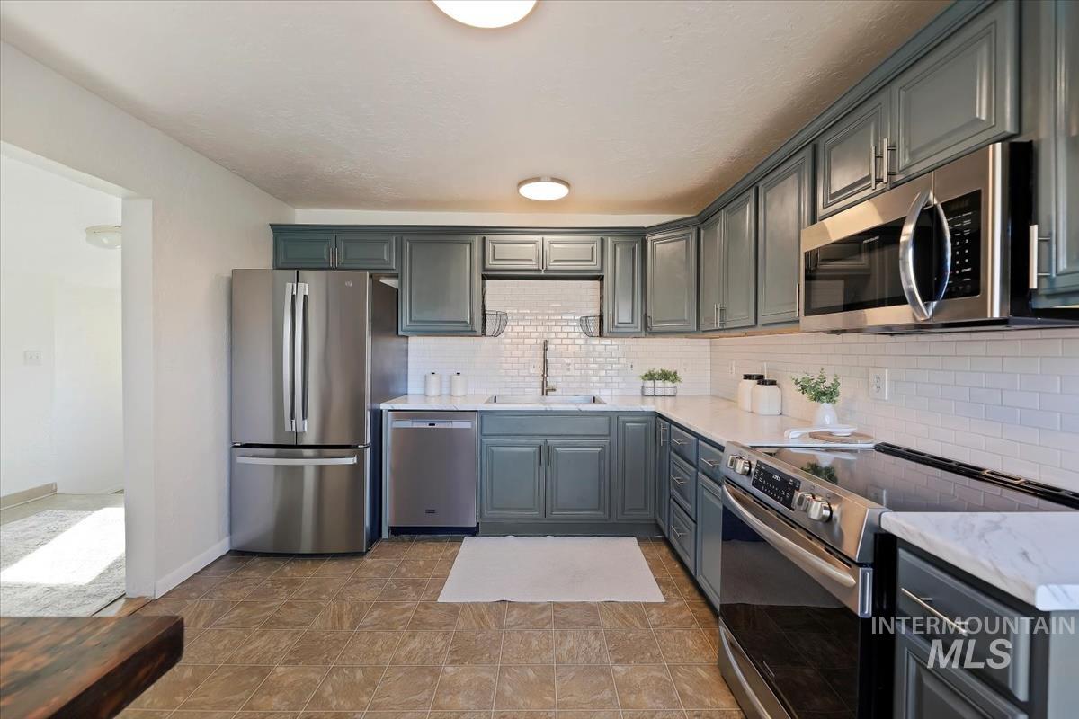 Kitchen featuring stainless steel appliances, light stone countertops, gray cabinets, and tasteful backsplash