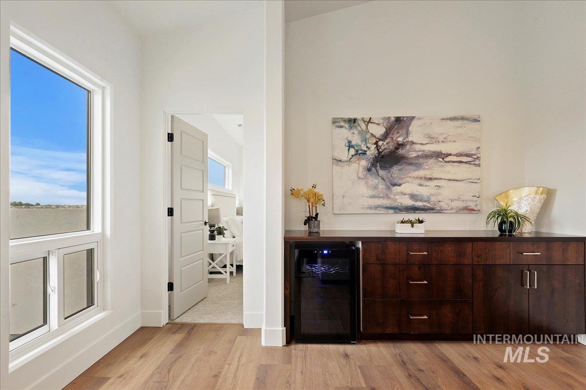 Bar area featuring wine cooler, dark brown cabinets, and light wood-style flooring