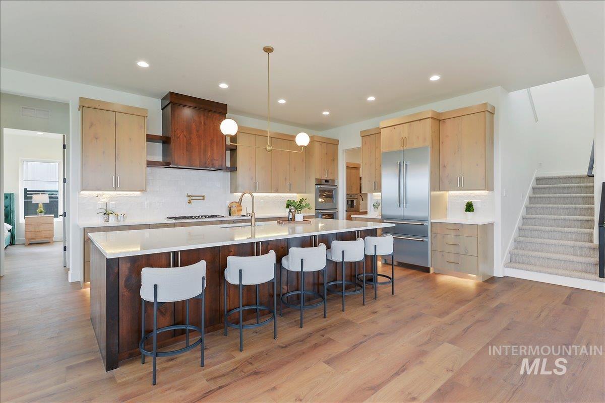 Kitchen with light brown cabinets, a large island with sink, a kitchen breakfast bar, stainless steel appliances, and pendant lighting