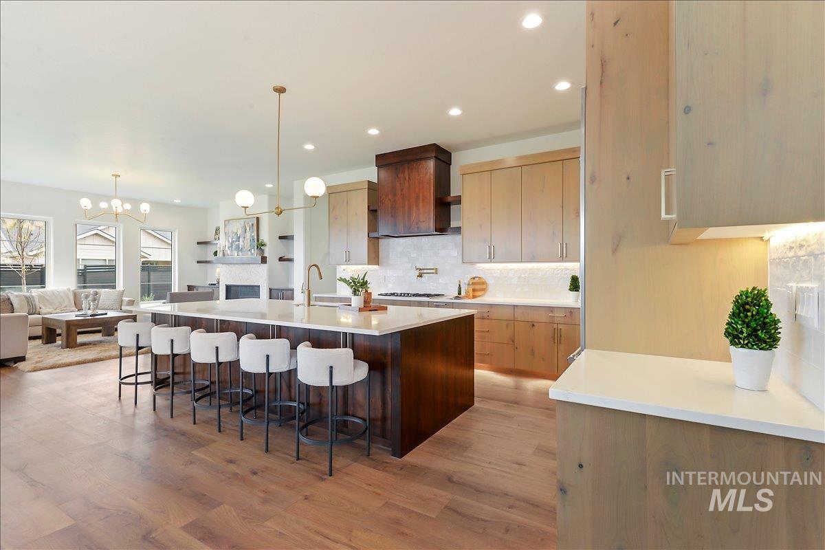 Kitchen featuring a chandelier, a center island with sink, backsplash, a breakfast bar, and light stone countertops