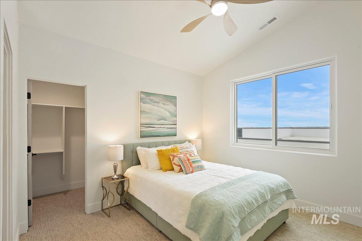 Bedroom with vaulted ceiling, a spacious closet, light colored carpet, and ceiling fan