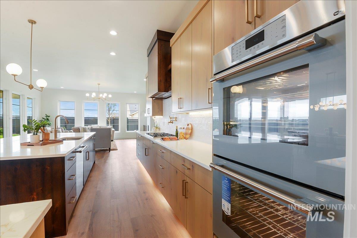 Kitchen featuring stainless steel appliances, light wood-style floors, hanging light fixtures, backsplash, and recessed lighting