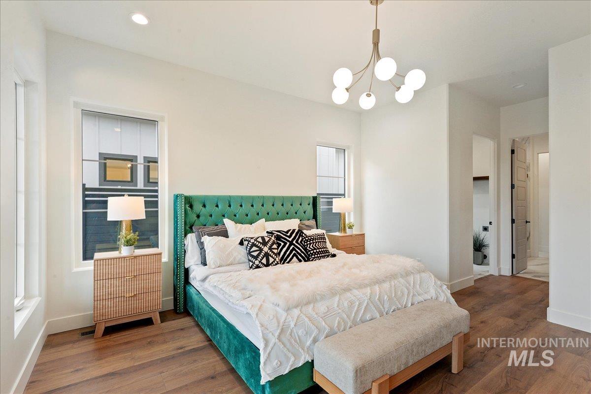 Bedroom with wood finished floors, a chandelier, ensuite bath, and recessed lighting
