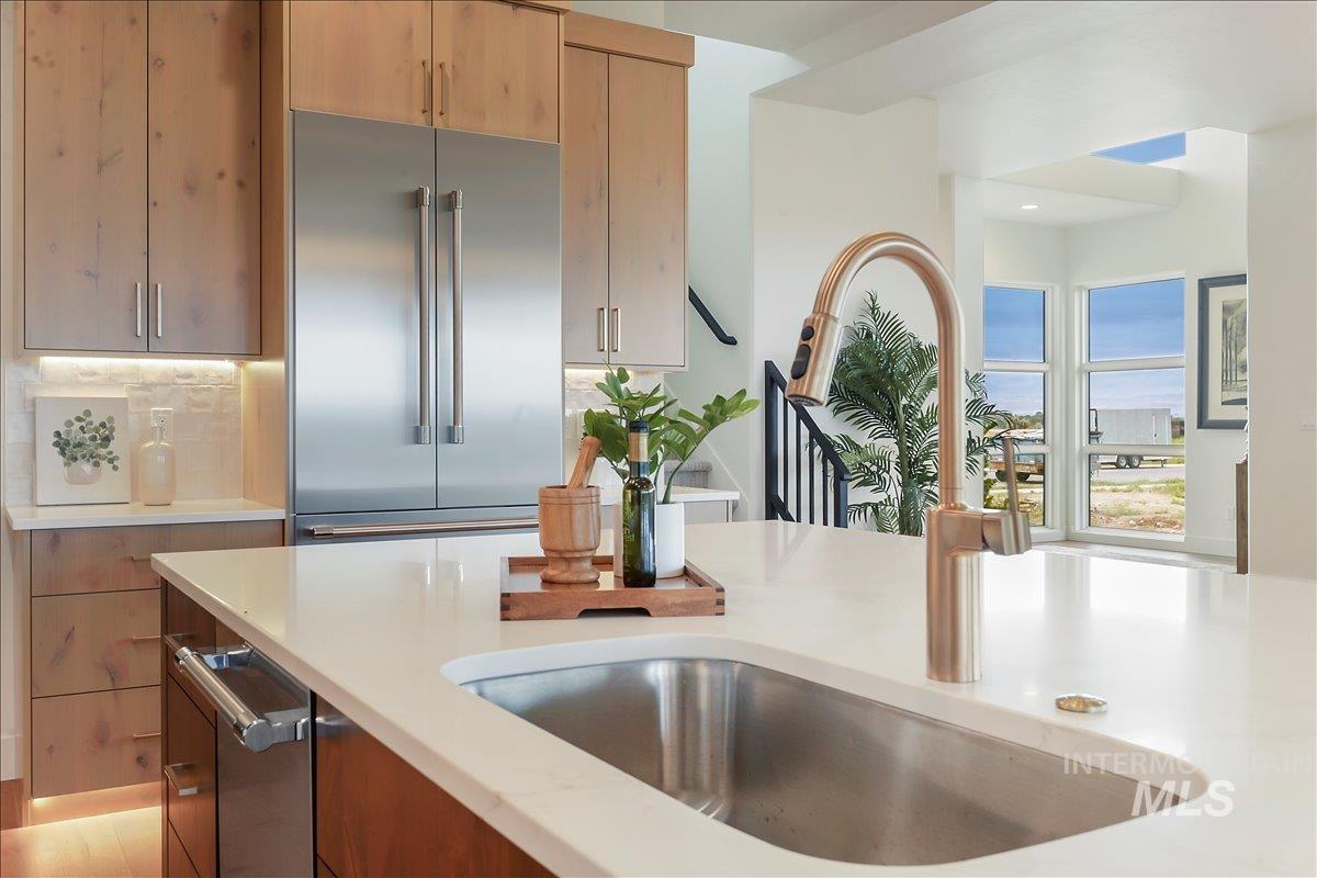 Kitchen with stainless steel built in refrigerator, light stone counters, brown cabinetry, and modern cabinets