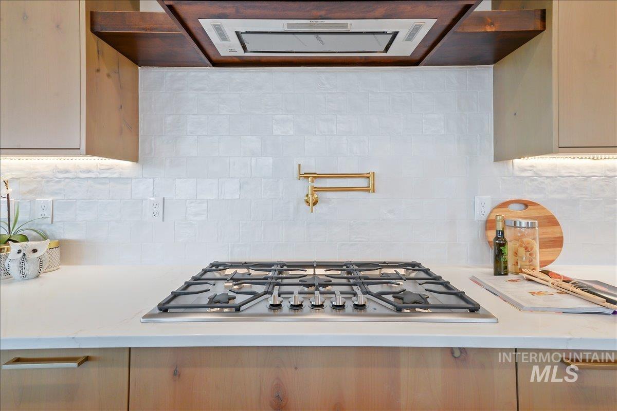 Kitchen featuring ventilation hood, backsplash, stainless steel gas cooktop, and light stone counters