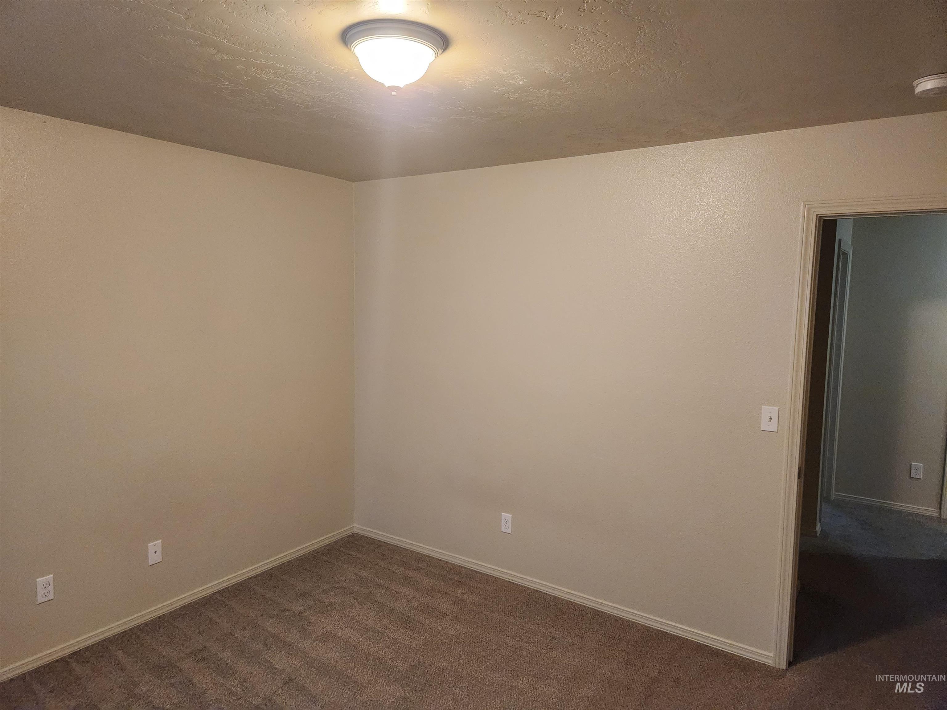 Empty room with a textured ceiling and dark colored carpet