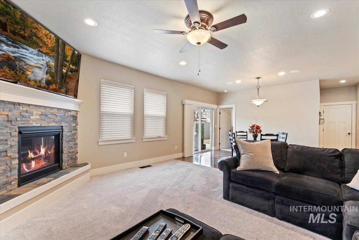 Carpeted living room featuring a stone fireplace, a ceiling fan, and recessed lighting