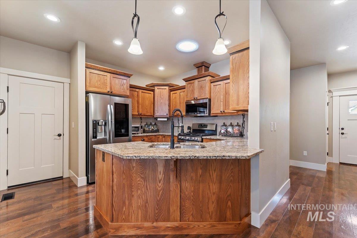 Kitchen featuring stainless steel appliances, light stone counters, a peninsula, brown cabinets, and hanging light fixtures