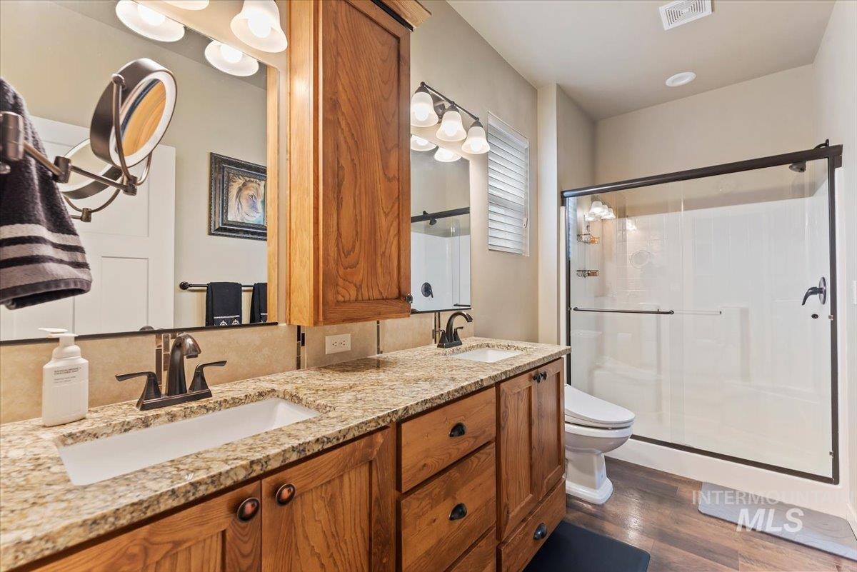 Full bath with double vanity, a stall shower, and dark wood-style floors