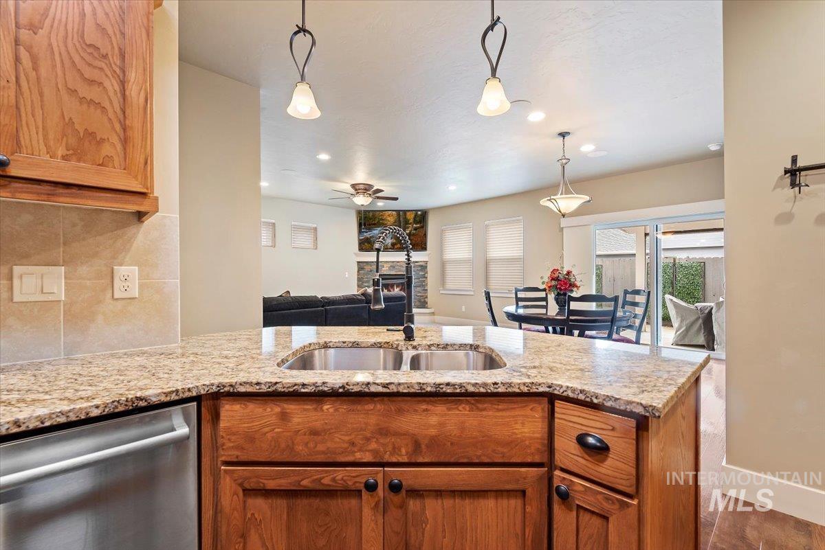 Kitchen with brown cabinets, light stone countertops, dishwasher, and recessed lighting