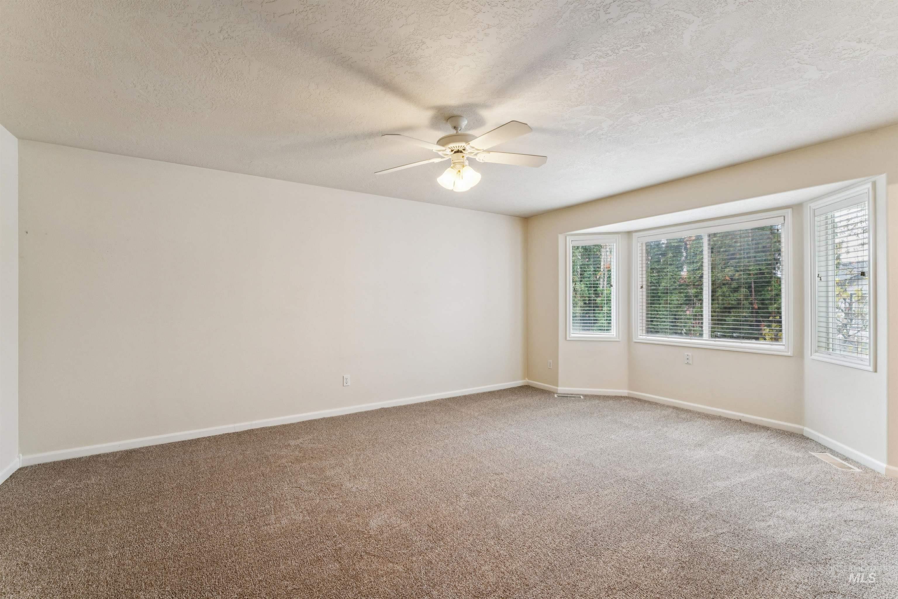 Carpeted empty room featuring a textured ceiling and ceiling fan