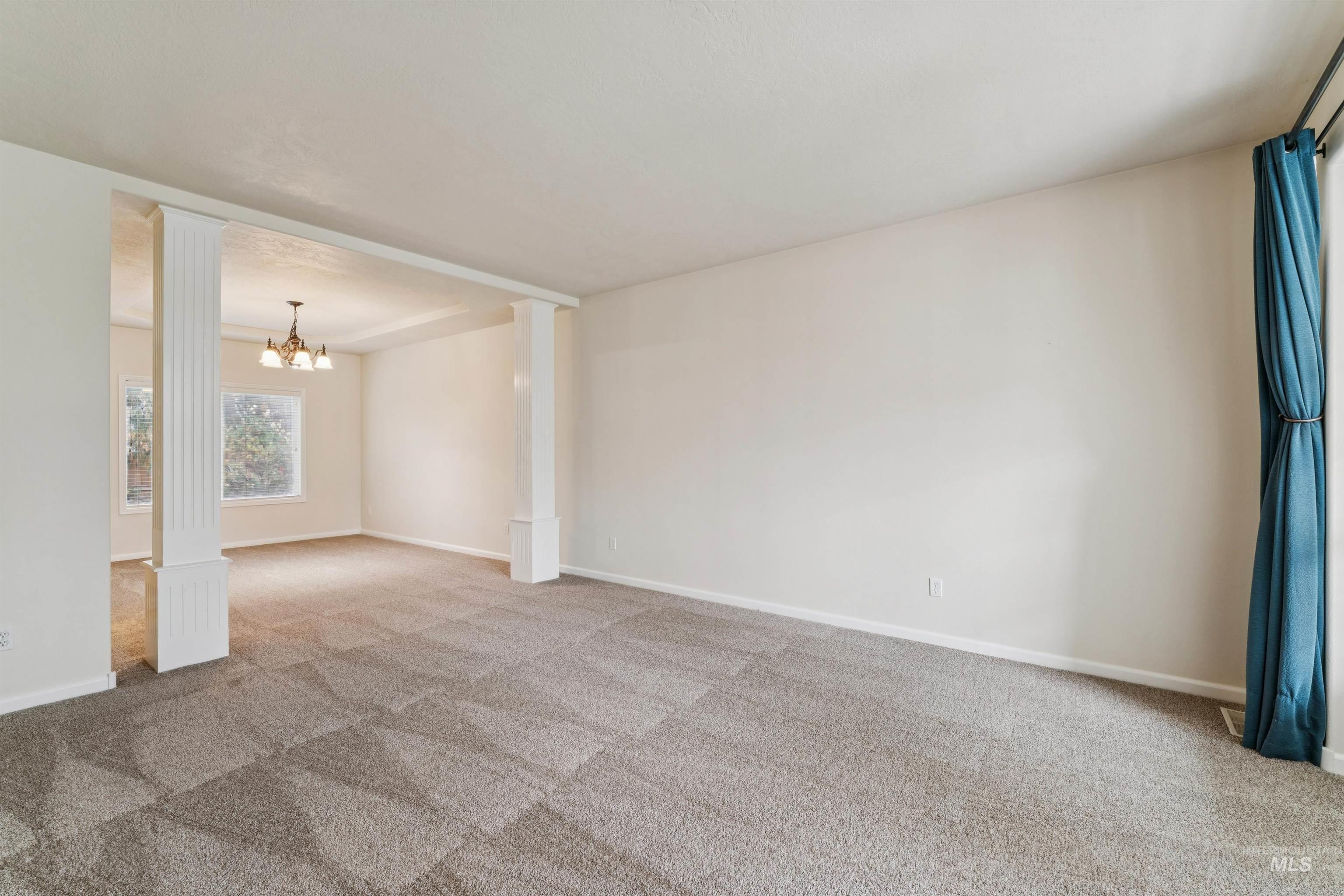 Empty room featuring a chandelier, carpet flooring, and ornate columns