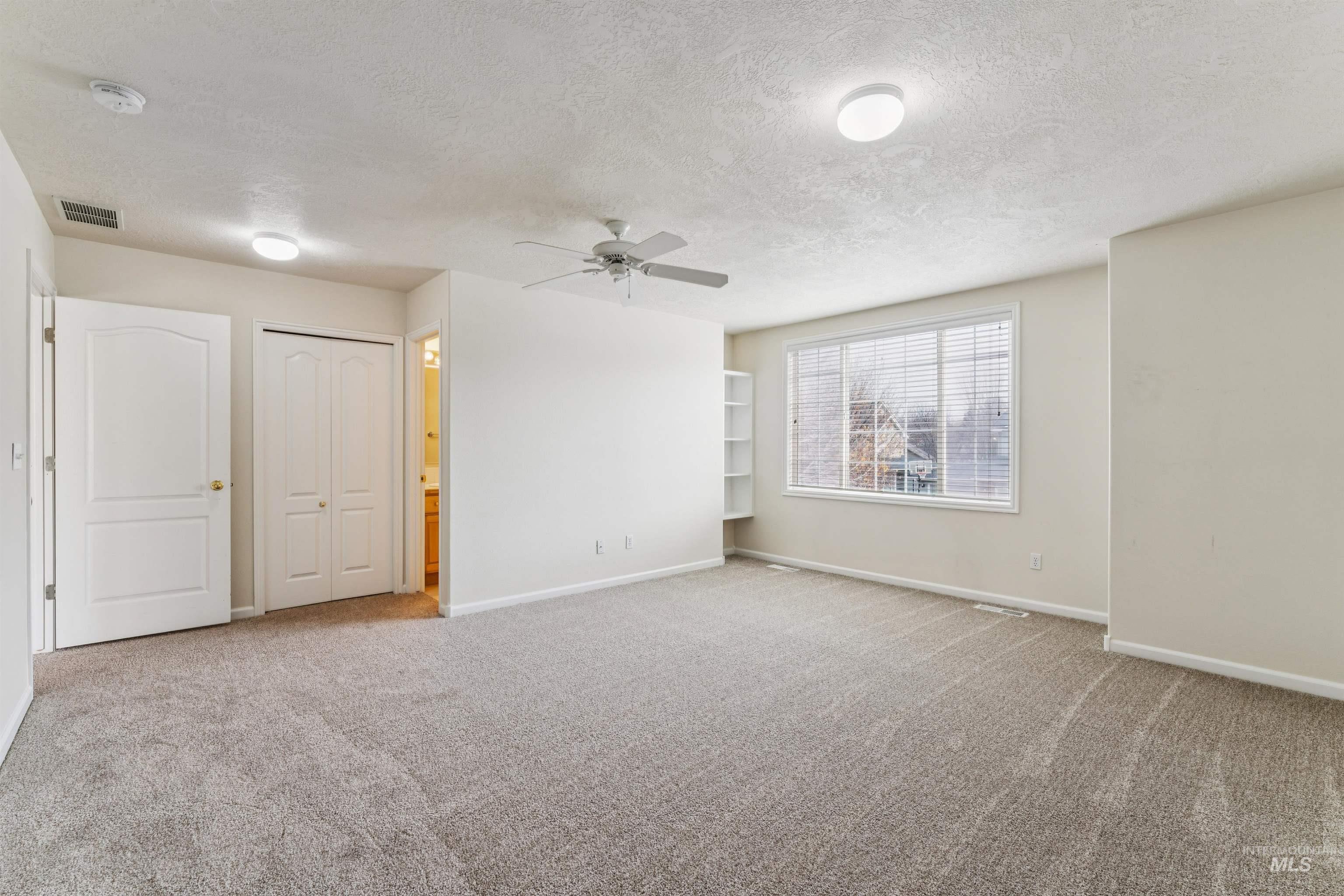 Unfurnished room featuring a textured ceiling, light colored carpet, and a ceiling fan