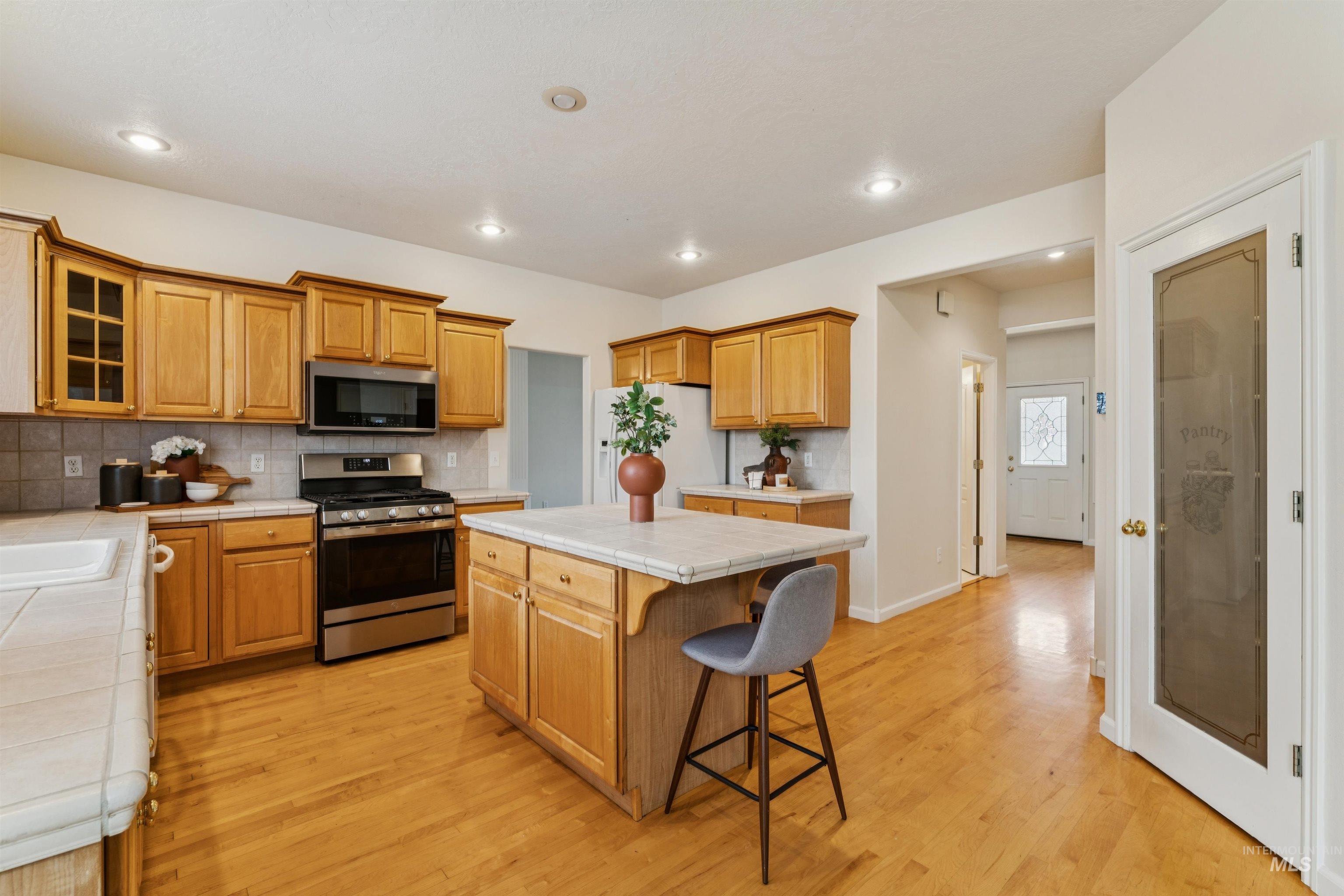 Kitchen featuring tile countertops, appliances with stainless steel finishes, a kitchen bar, a kitchen island, and tasteful backsplash