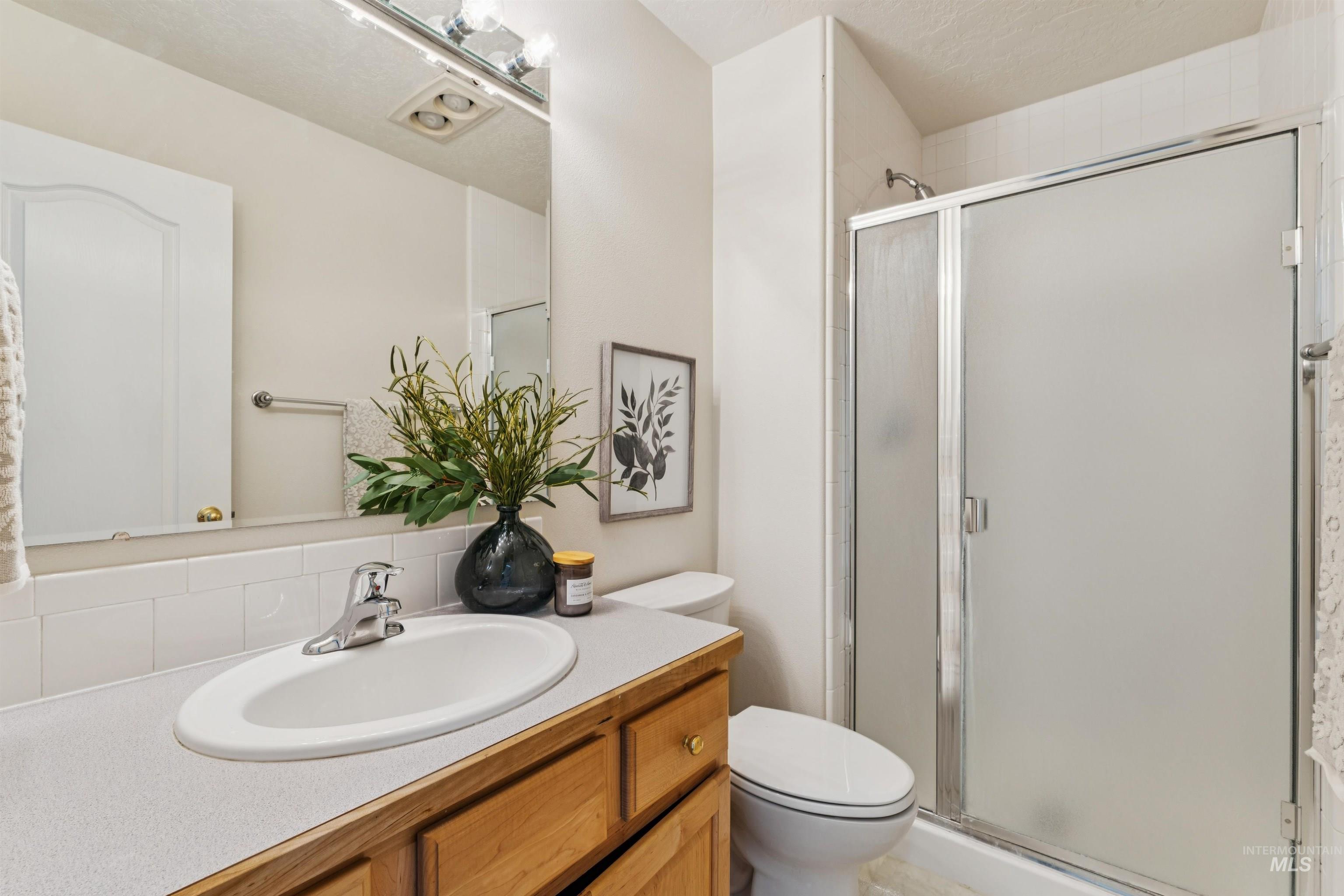 Full bath with vanity, a stall shower, backsplash, and a textured ceiling