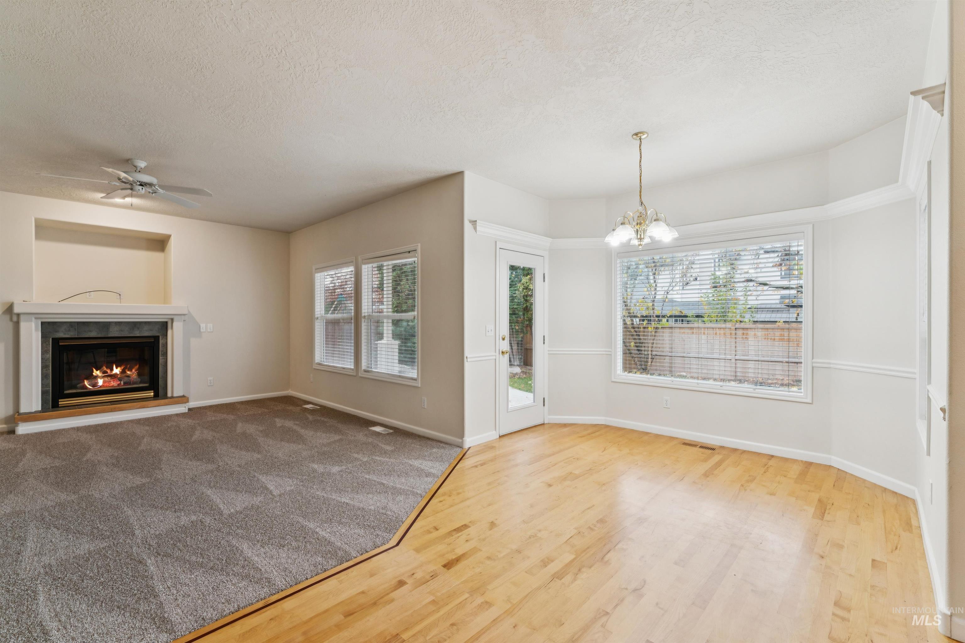 Unfurnished living room with a textured ceiling, a chandelier, a fireplace, light wood-type flooring, and a ceiling fan