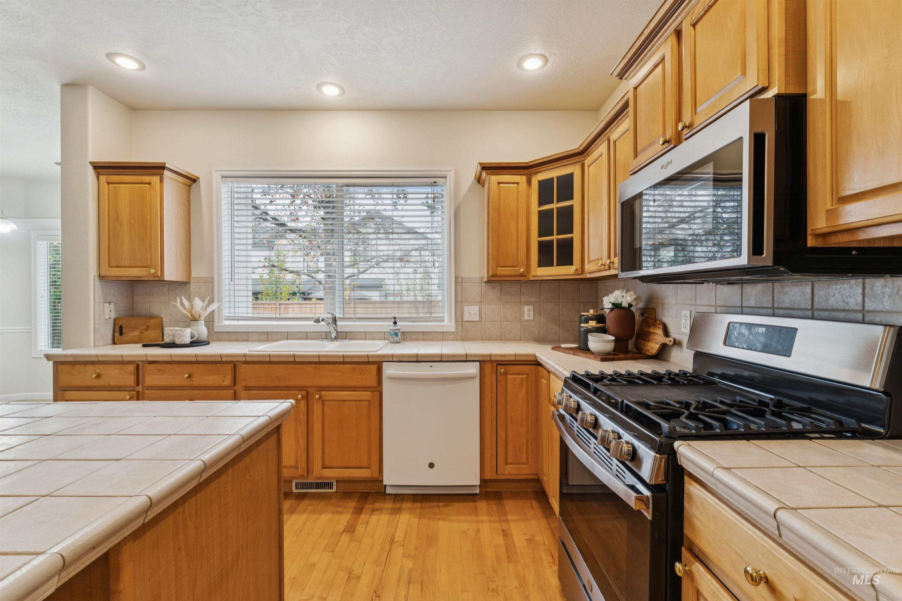 Kitchen with appliances with stainless steel finishes, tile counters, light wood-style flooring, decorative backsplash, and recessed lighting