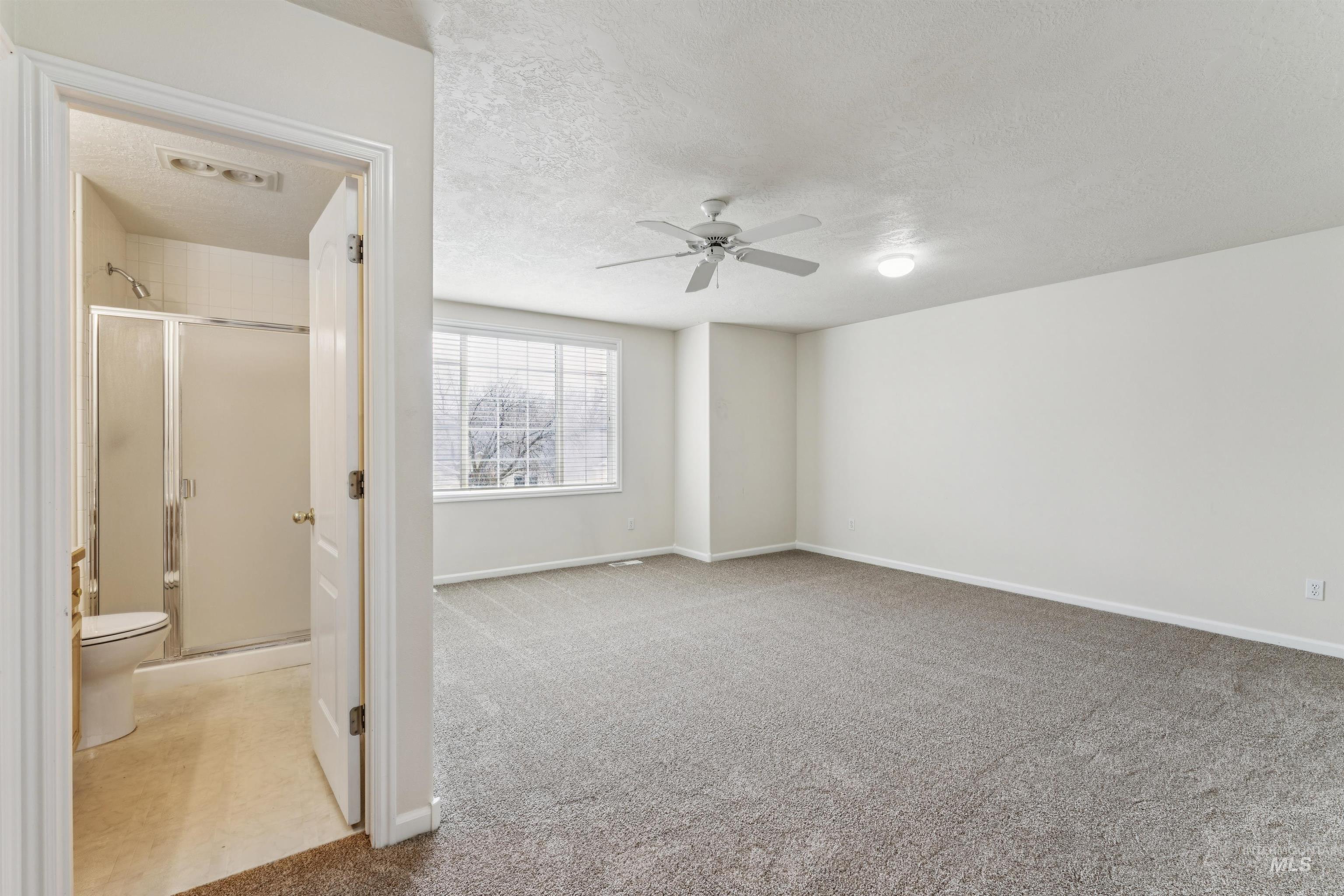Empty room with light colored carpet, a textured ceiling, and ceiling fan