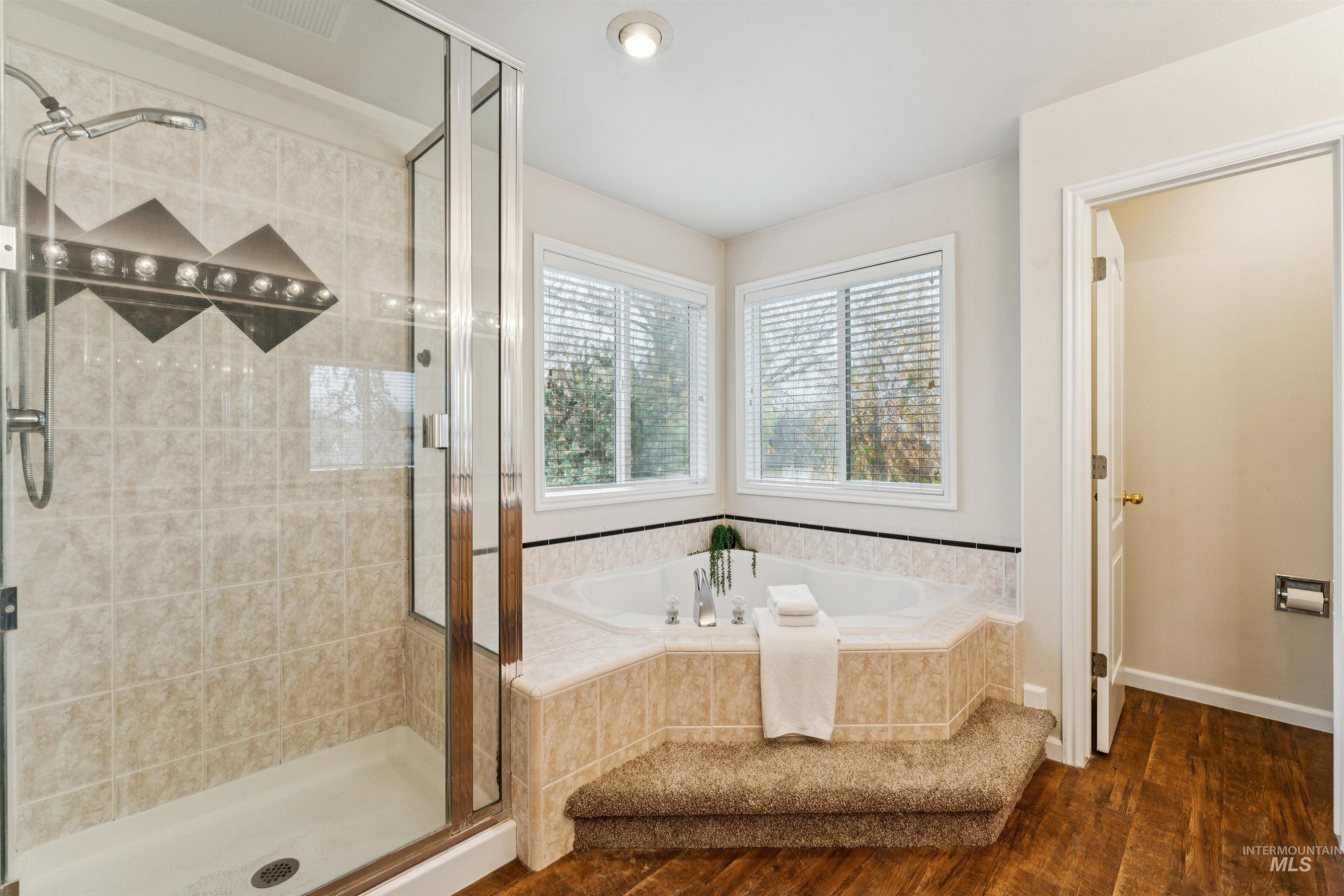 Bathroom with a stall shower, dark wood-type flooring, and a garden tub