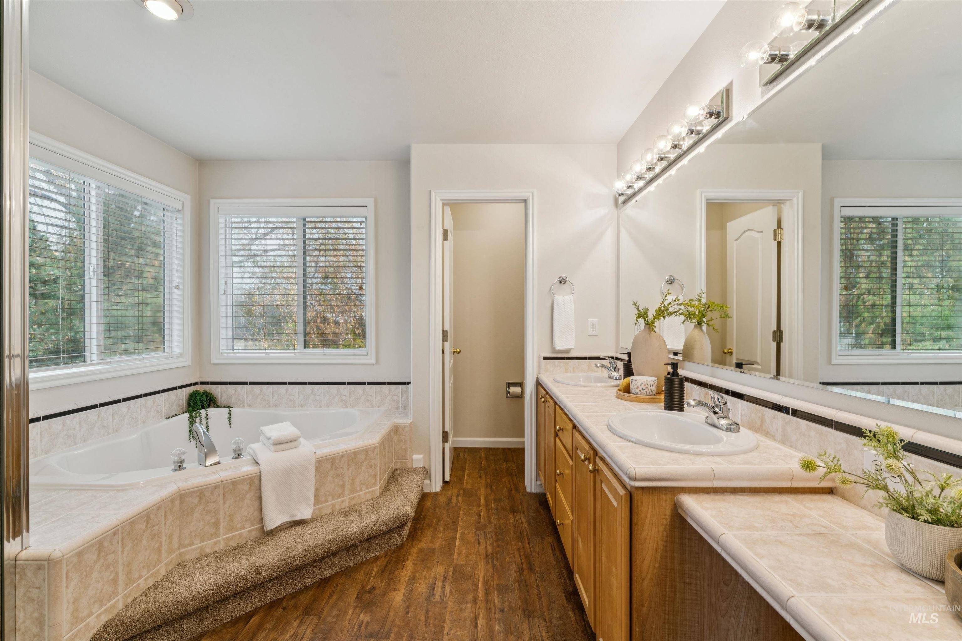Full bathroom featuring double vanity, a garden tub, healthy amount of natural light, and dark wood-style flooring