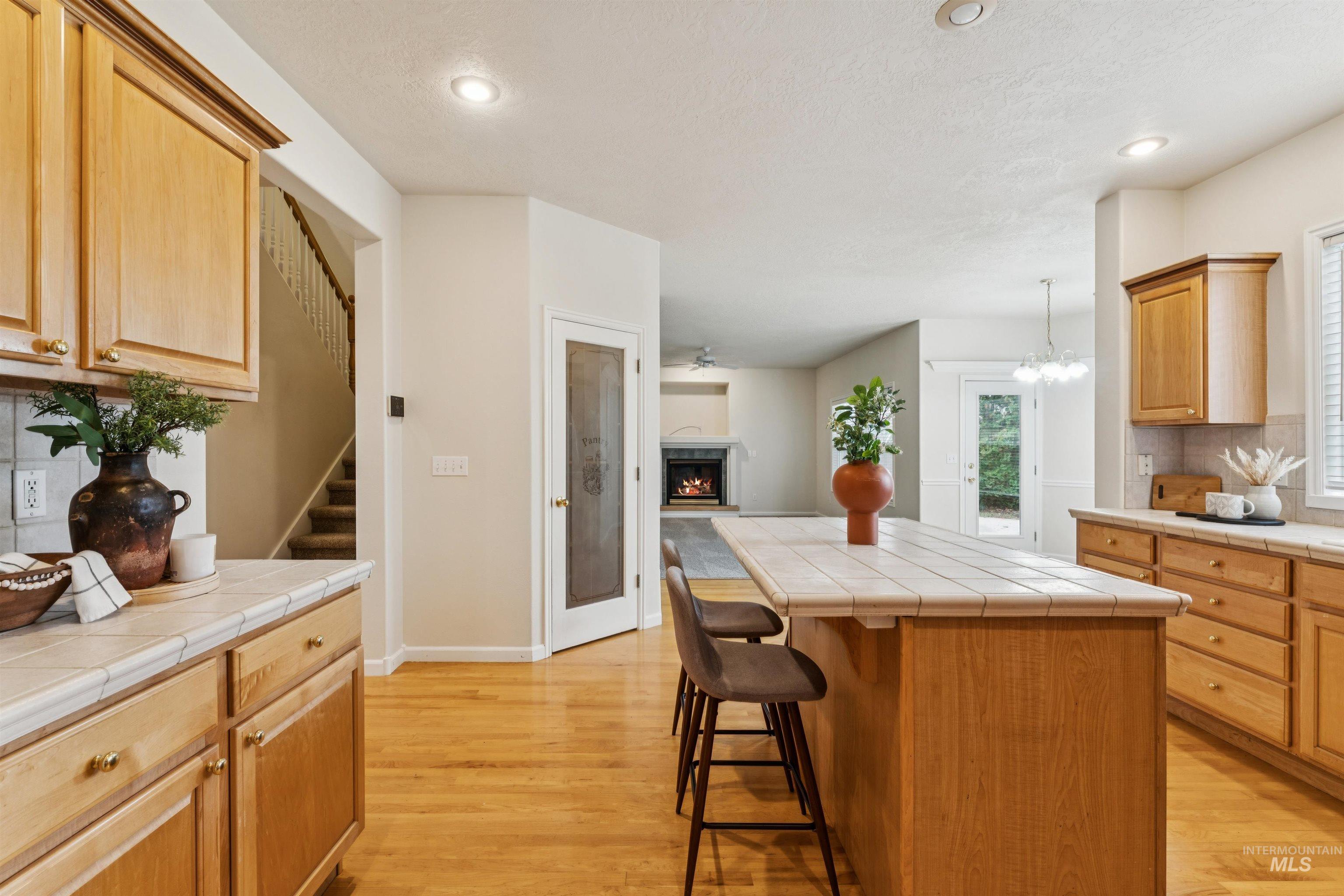 Kitchen with tasteful backsplash, tile counters, a kitchen breakfast bar, a warm lit fireplace, and light wood-style floors