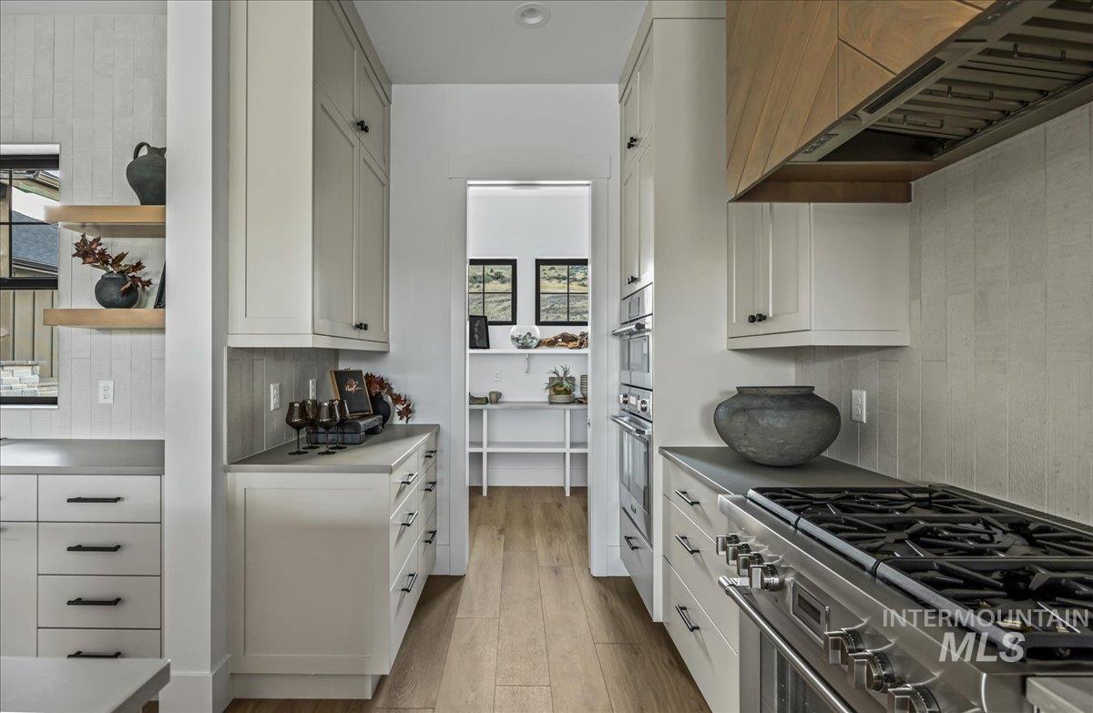 Kitchen with open shelves, stainless steel appliances, exhaust hood, light wood-style flooring, and white cabinetry