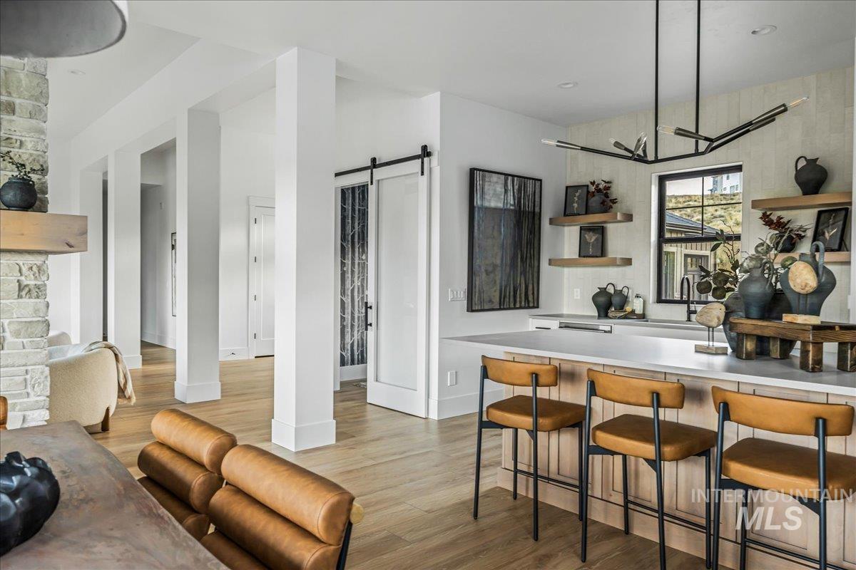 Bar with light countertops, open shelves, a barn door, and light wood-style floors
