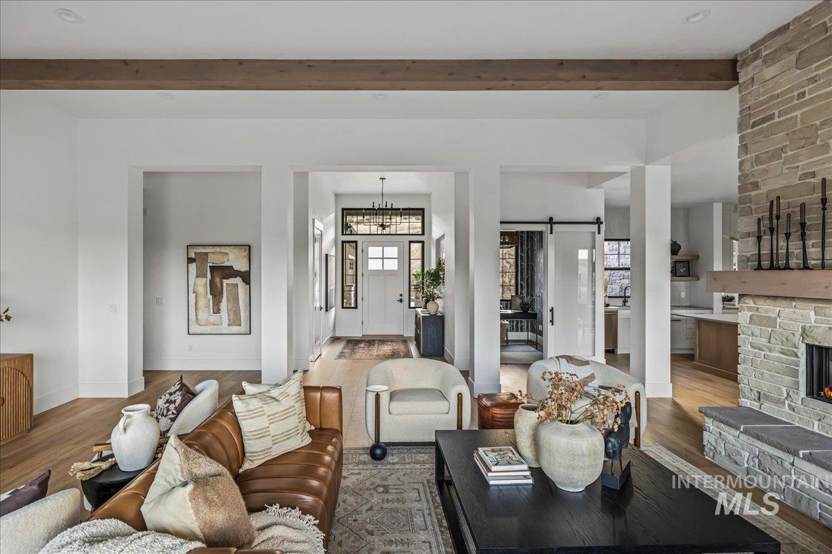 Living area featuring a barn door, wood finished floors, beamed ceiling, a chandelier, and a stone fireplace