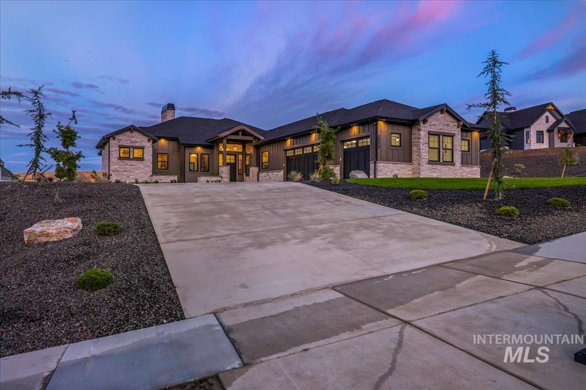 View of front of house featuring stone siding, concrete driveway, a chimney, and board and batten siding