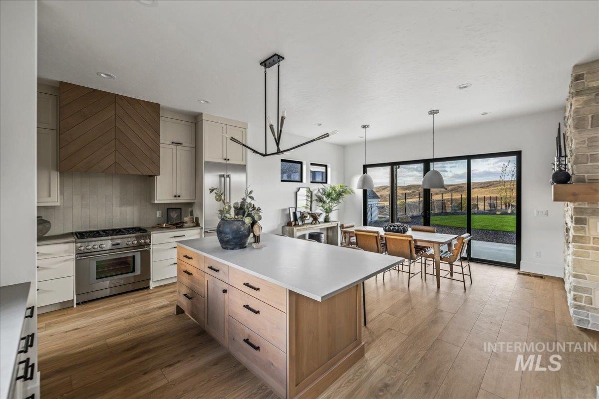 Kitchen featuring high end appliances, hanging light fixtures, light wood finished floors, wall chimney range hood, and a center island