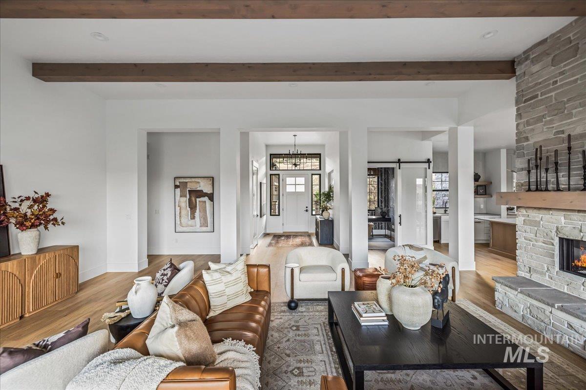 Living area featuring a barn door, wood finished floors, a chandelier, beam ceiling, and a stone fireplace