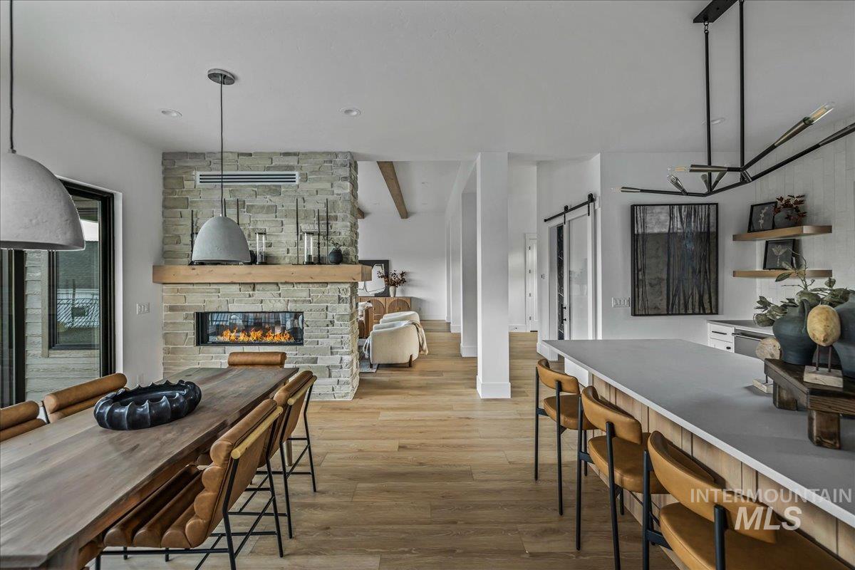 Dining area with a fireplace, light wood-type flooring, a barn door, and beamed ceiling