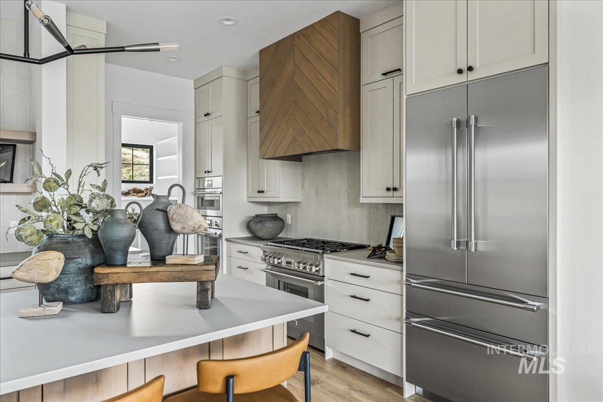 Kitchen featuring premium appliances, wall chimney exhaust hood, light countertops, white cabinets, and light wood-style flooring