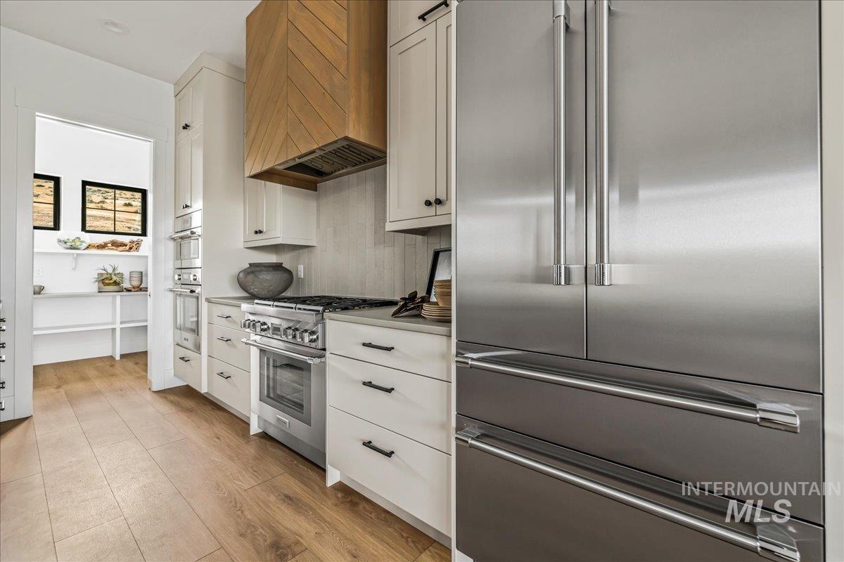 Kitchen with high quality appliances, custom range hood, light wood-type flooring, white cabinetry, and light countertops