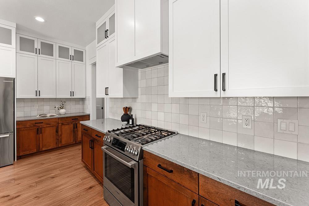 Kitchen featuring stainless steel appliances, white cabinets, light stone counters, decorative backsplash, and light wood-style flooring