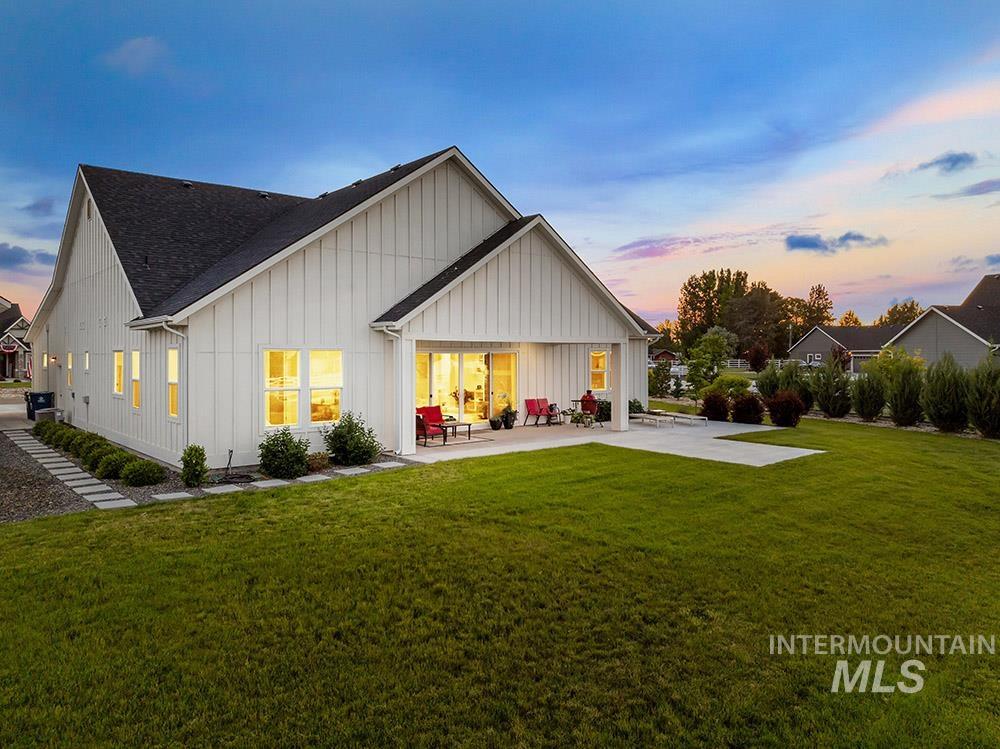 Rear view of house with a patio area, board and batten siding, a yard, and roof with shingles