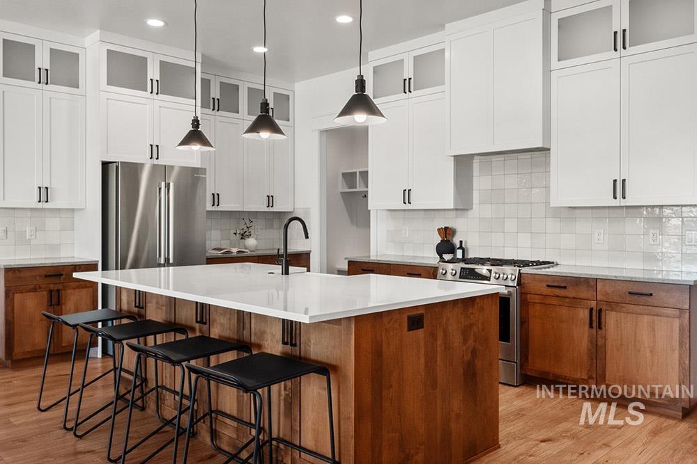 Kitchen with stainless steel appliances, decorative backsplash, an island with sink, light countertops, and recessed lighting