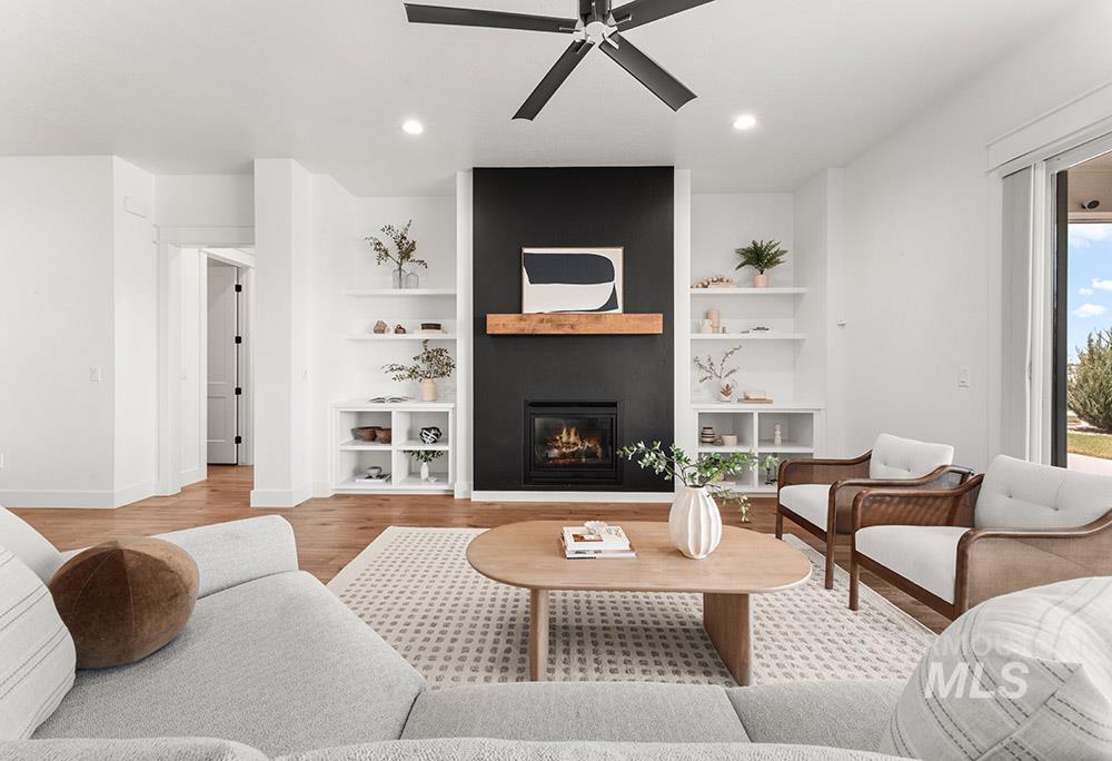 Living room featuring ceiling fan, built in features, a large fireplace, wood finished floors, and recessed lighting