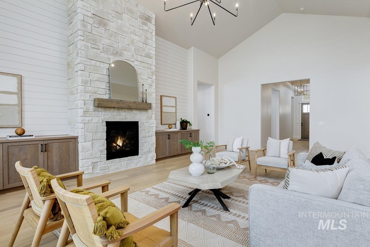 Living room with a chandelier, high vaulted ceiling, a stone fireplace, wood finished floors, and wooden walls