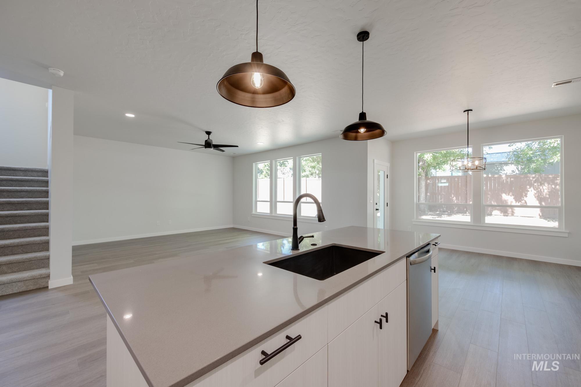 Kitchen with dishwasher, light wood-style floors, white cabinetry, hanging light fixtures, and an island with sink