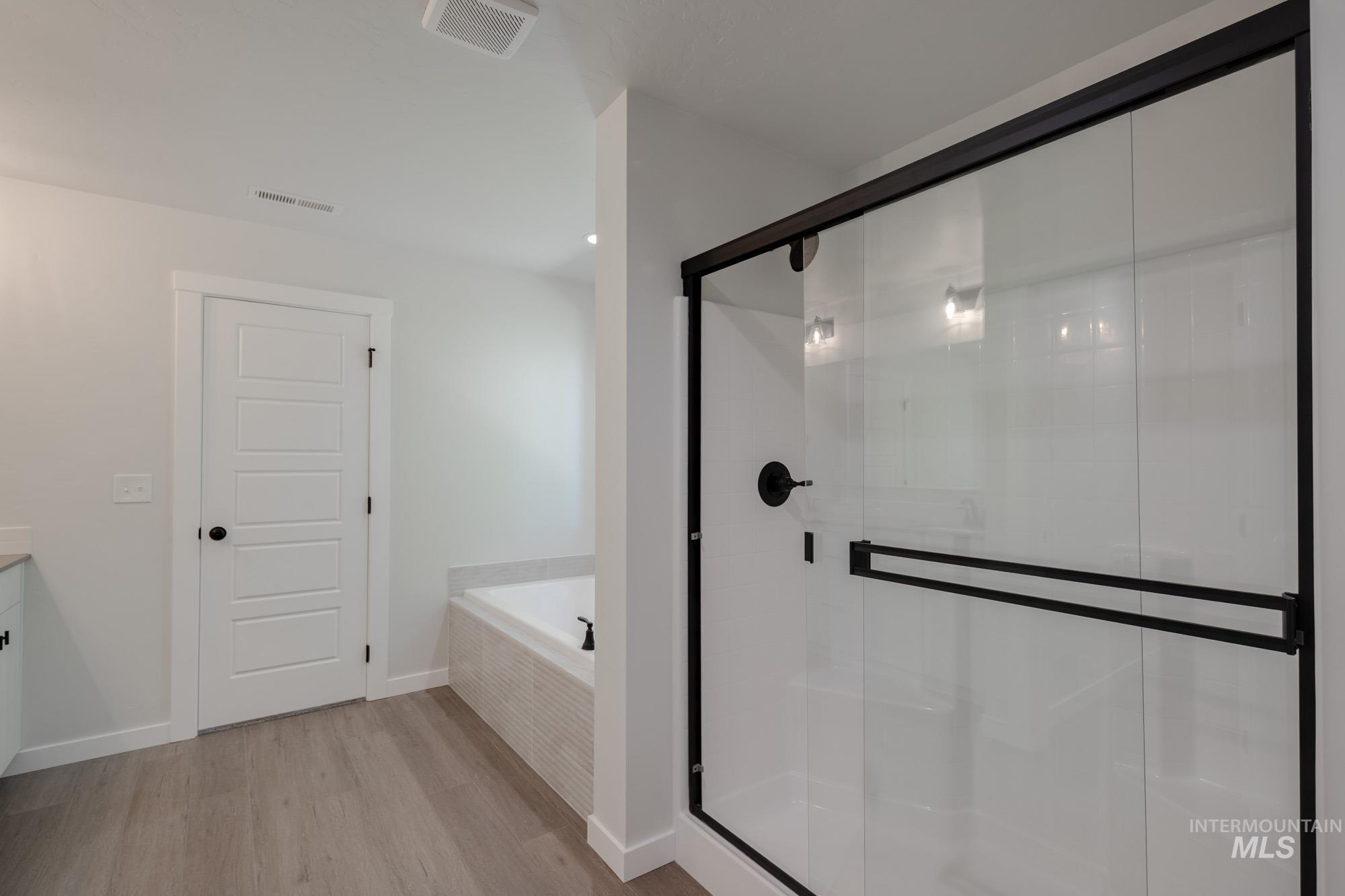 Full bathroom featuring wood finished floors, a bath, a shower stall, and vanity