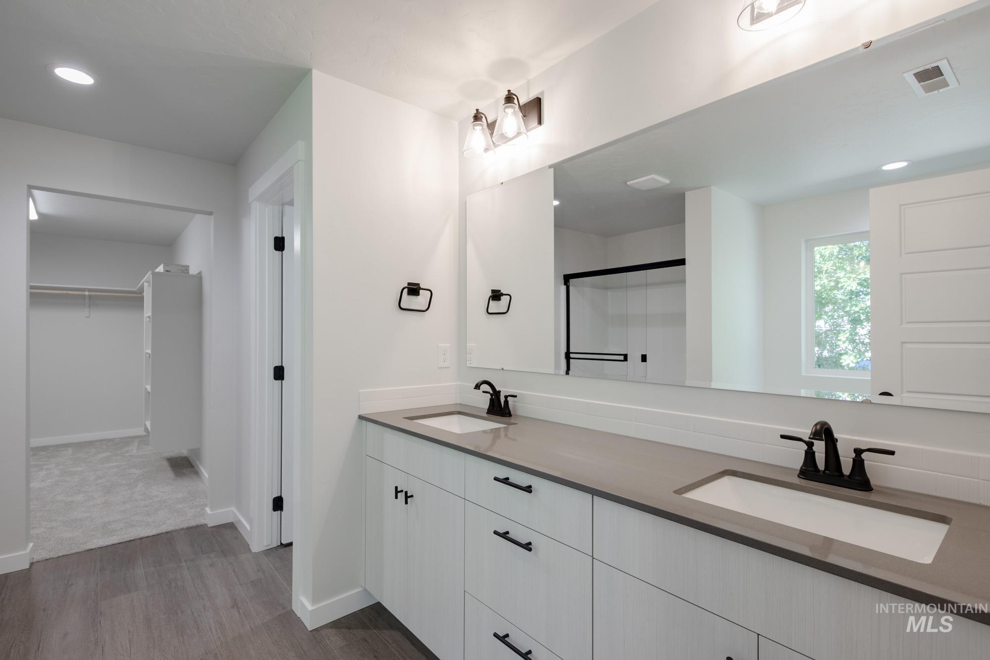 Full bath with double vanity, wood finished floors, a spacious closet, an enclosed shower, and recessed lighting