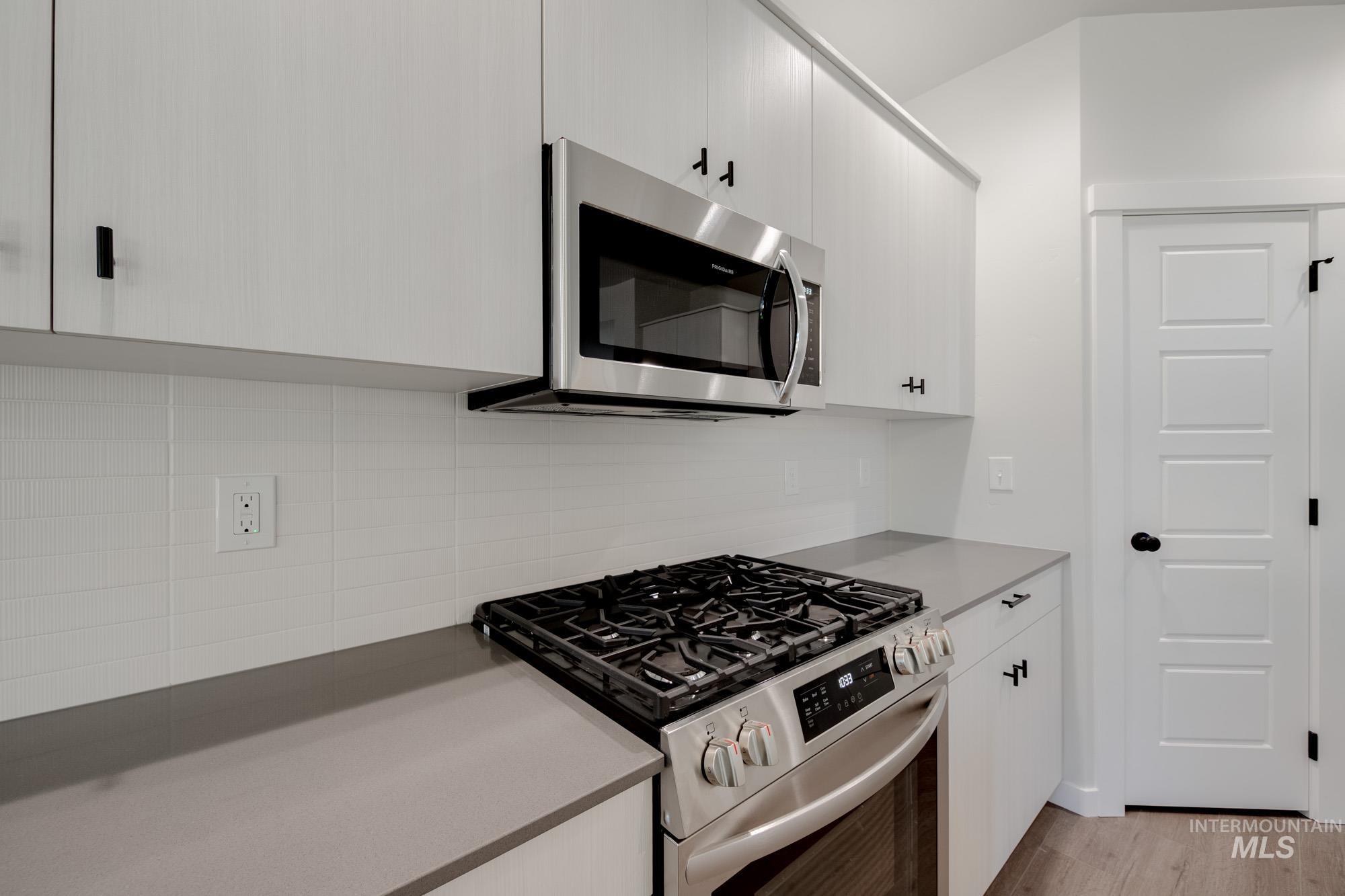 Kitchen with appliances with stainless steel finishes, decorative backsplash, light wood-style flooring, and white cabinets