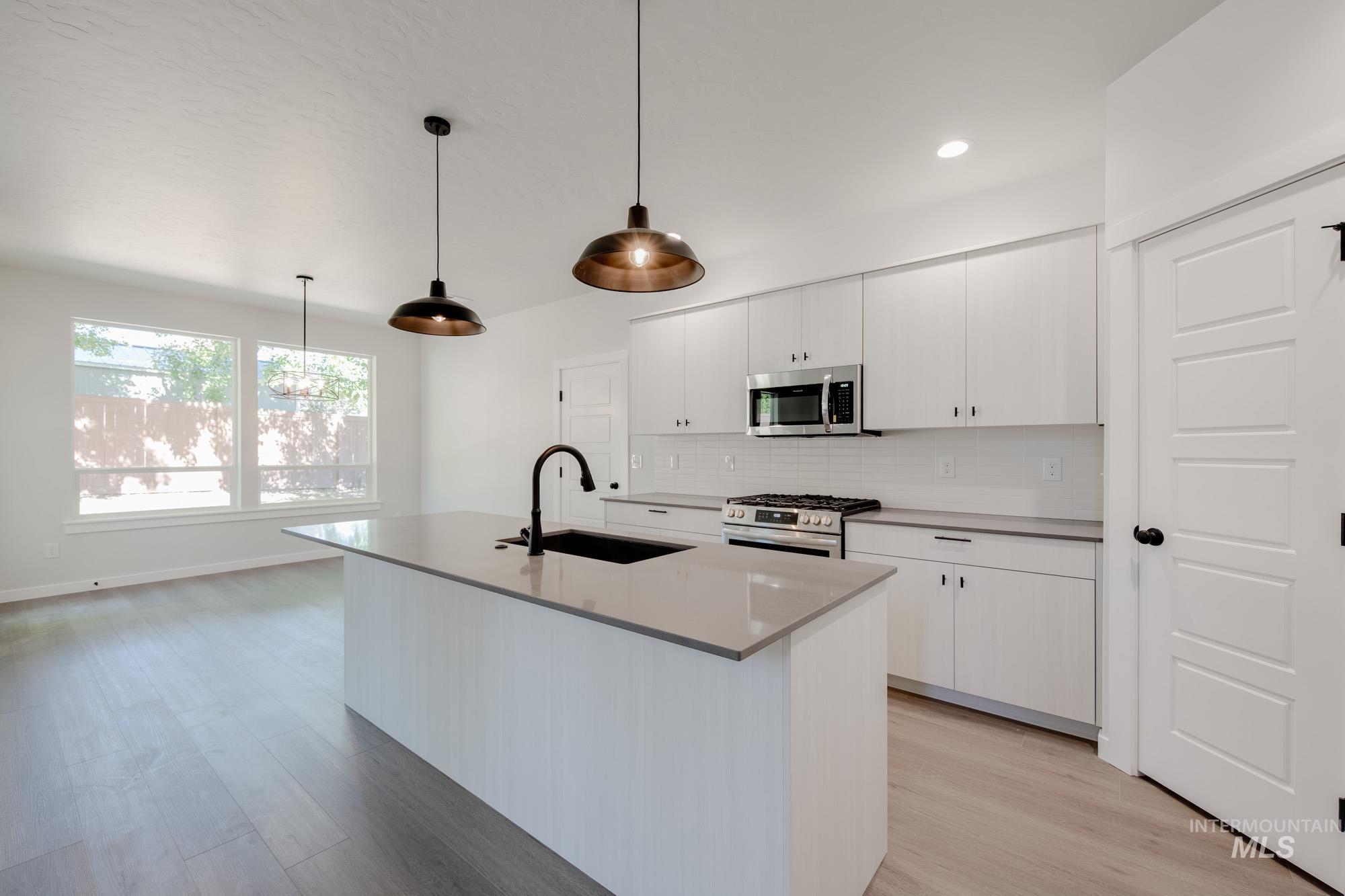Kitchen with stainless steel appliances, light wood-style flooring, backsplash, white cabinetry, and hanging light fixtures