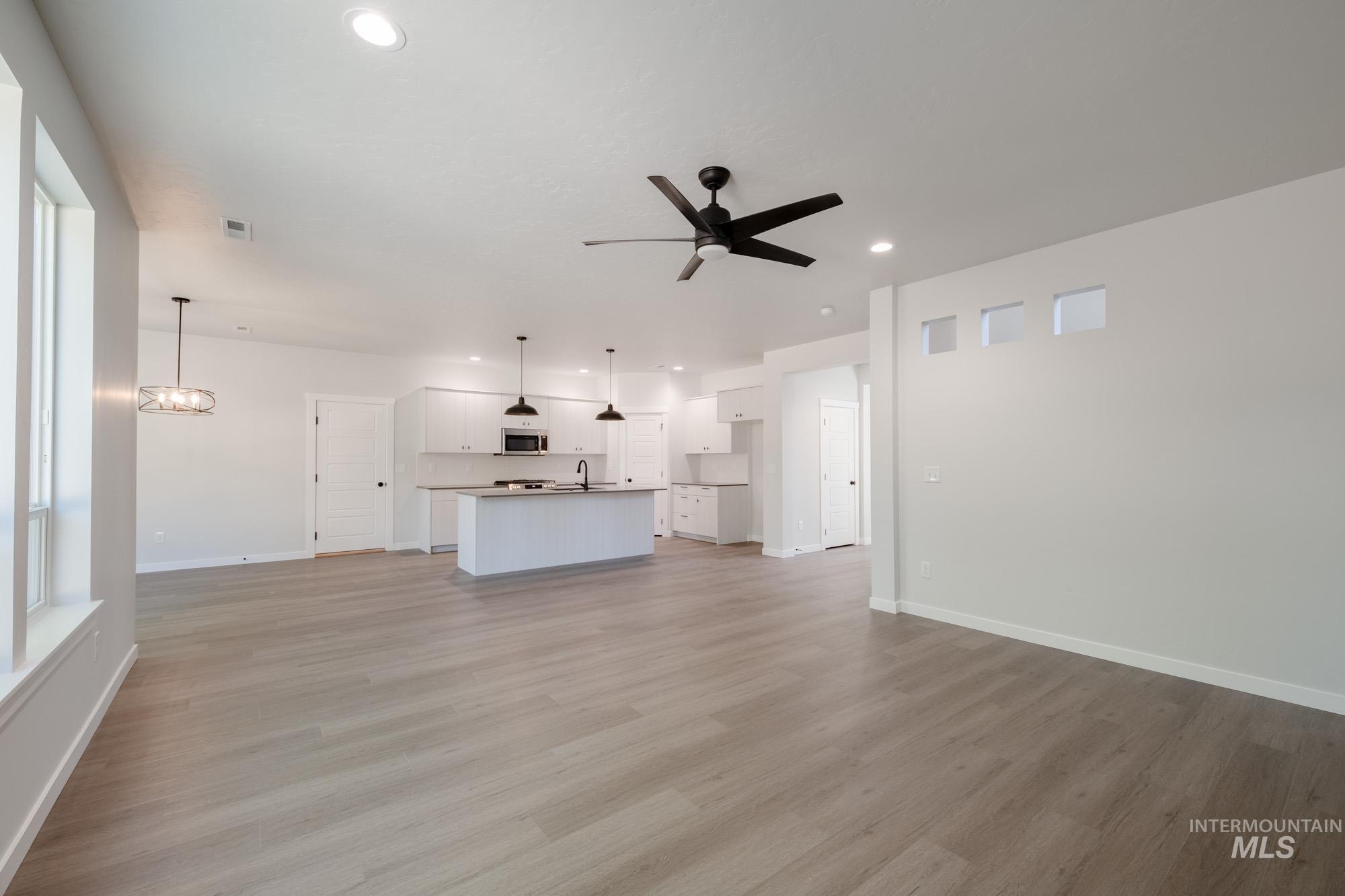Unfurnished living room with ceiling fan, light wood finished floors, recessed lighting, and a chandelier
